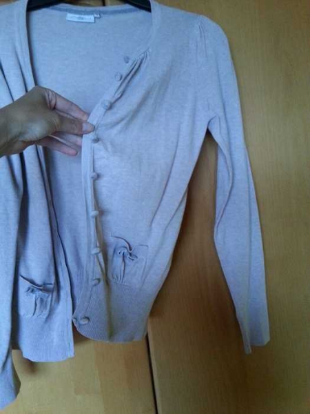 Beige Strickweste mit samtähnlichen Knöpfen und einem Schleifchen auf der Tasche