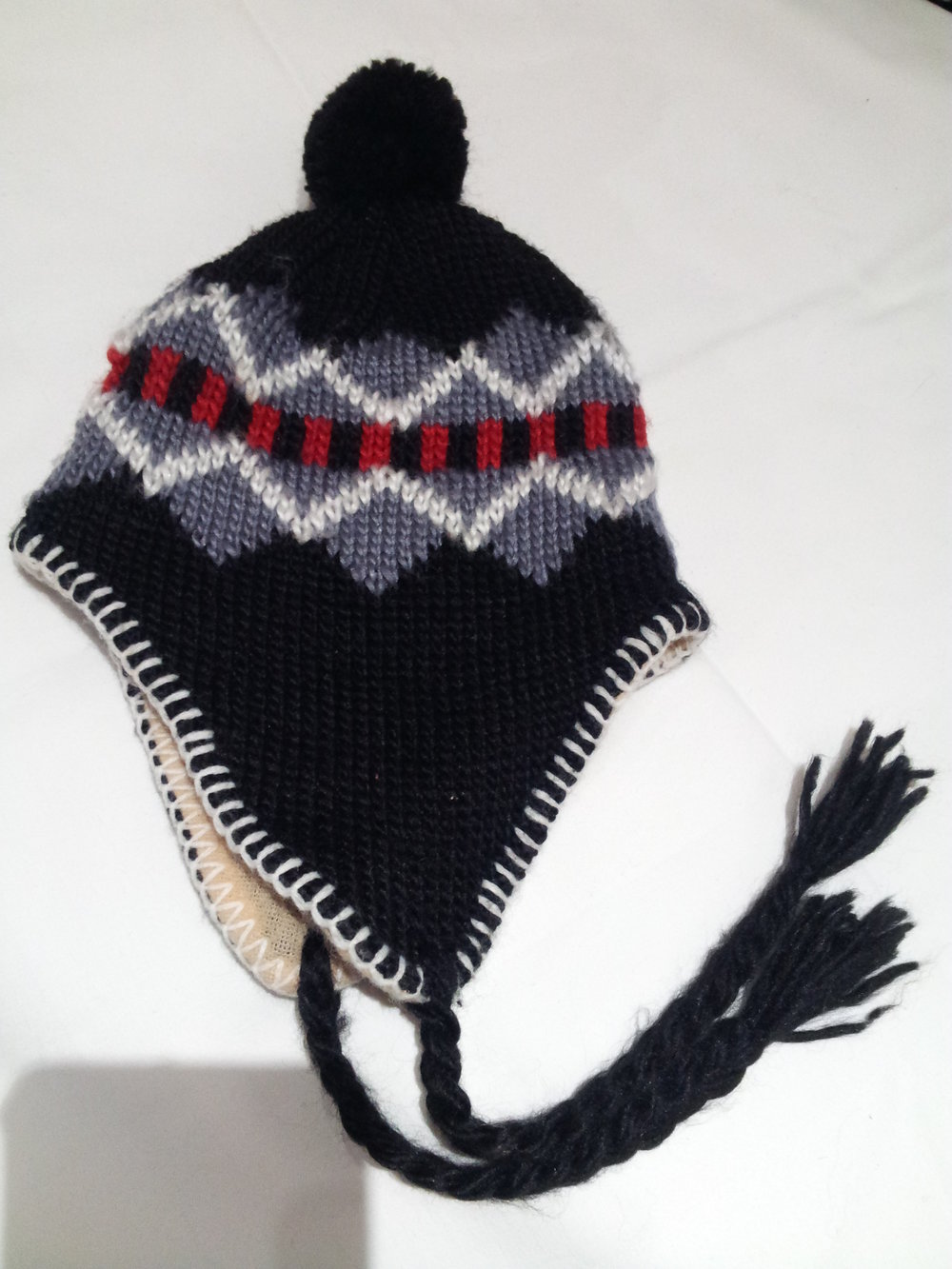 schwarze Wollmütze mit Ohrenklappen und Bommel