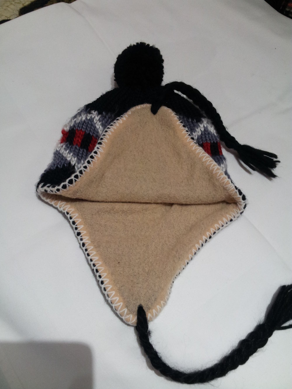 schwarze Wollmütze mit Ohrenklappen und Bommel