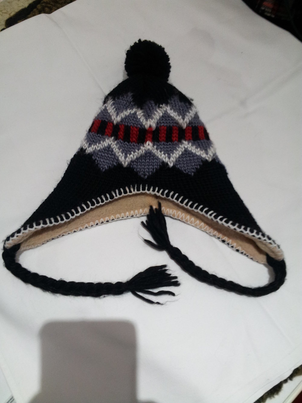 schwarze Wollmütze mit Ohrenklappen und Bommel