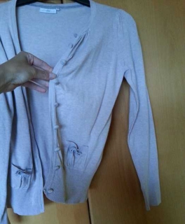 Beige Strickweste mit samtähnlichen Knöpfen und einem Schleifchen auf der Tasche